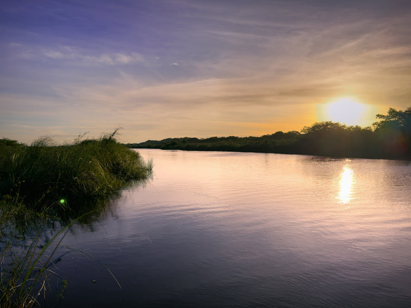 Sonnenuntergang über einem Fluss in Belize, warmes Licht spiegelt sich im Wasser.