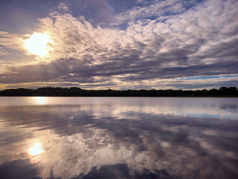 Ruhige Wasserfläche in Belize spiegelt Himmel und Wolken im warmen Licht.