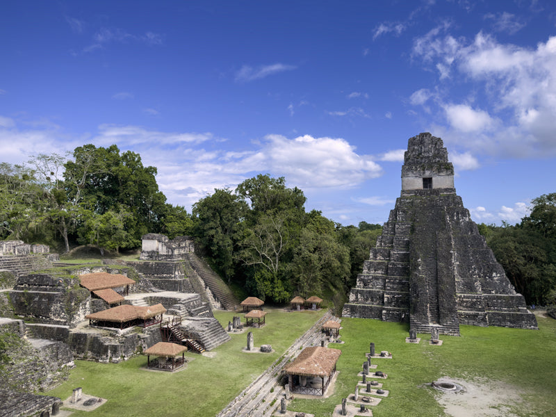 Maya-Tempel in Tikal mit offener Rasenfläche, kleinen Bauwerken und umliegendem Wald.