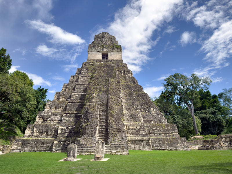Frontalansicht eines großen Maya-Tempels aus Stein in Tikal, umgeben von Grün und blauem Himmel.