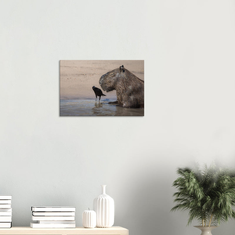 Mockup: Wasserschwein sitzt im flachen Wasser am Sandufer, daneben steht ein schwarzer Vogel, warme Lichtstimmung.